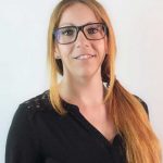 Eine Frau vom Einfachmarketing-Team lächelt vor einer weißen Wand.