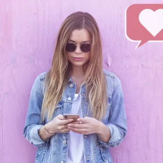 Eine Frau nutzt ein Mobiltelefon für Social-Media-Marketing vor einer rosa Wand.