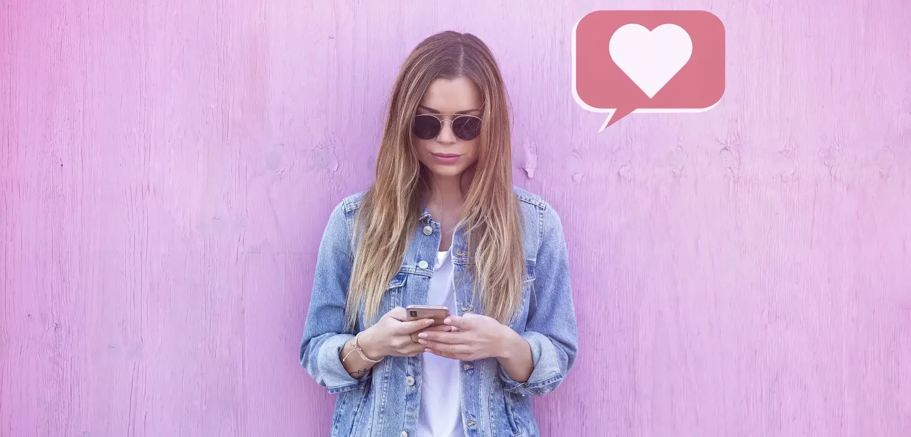 Eine Frau nutzt ein Mobiltelefon für Social-Media-Marketing vor einer rosa Wand.