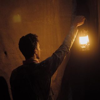 Ein visuell fesselndes Bild eines Mannes, der in einem dunklen Raum nach einem Licht greift, stellt die Kunst des Geschichtenerzählens perfekt dar.