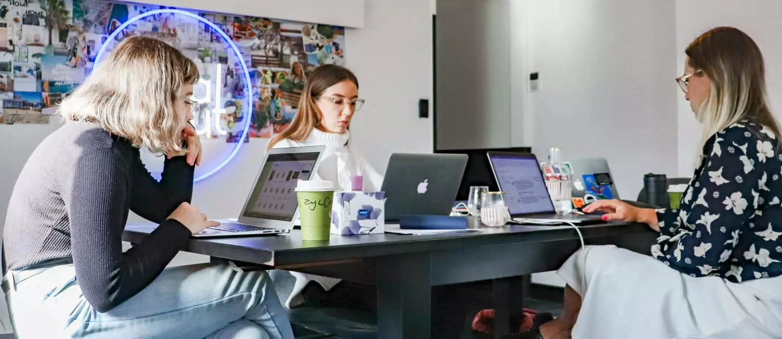 Eine Gruppe von Frauen nutzt Social-Media-Tools, während sie mit Laptops an einem Tisch sitzen.