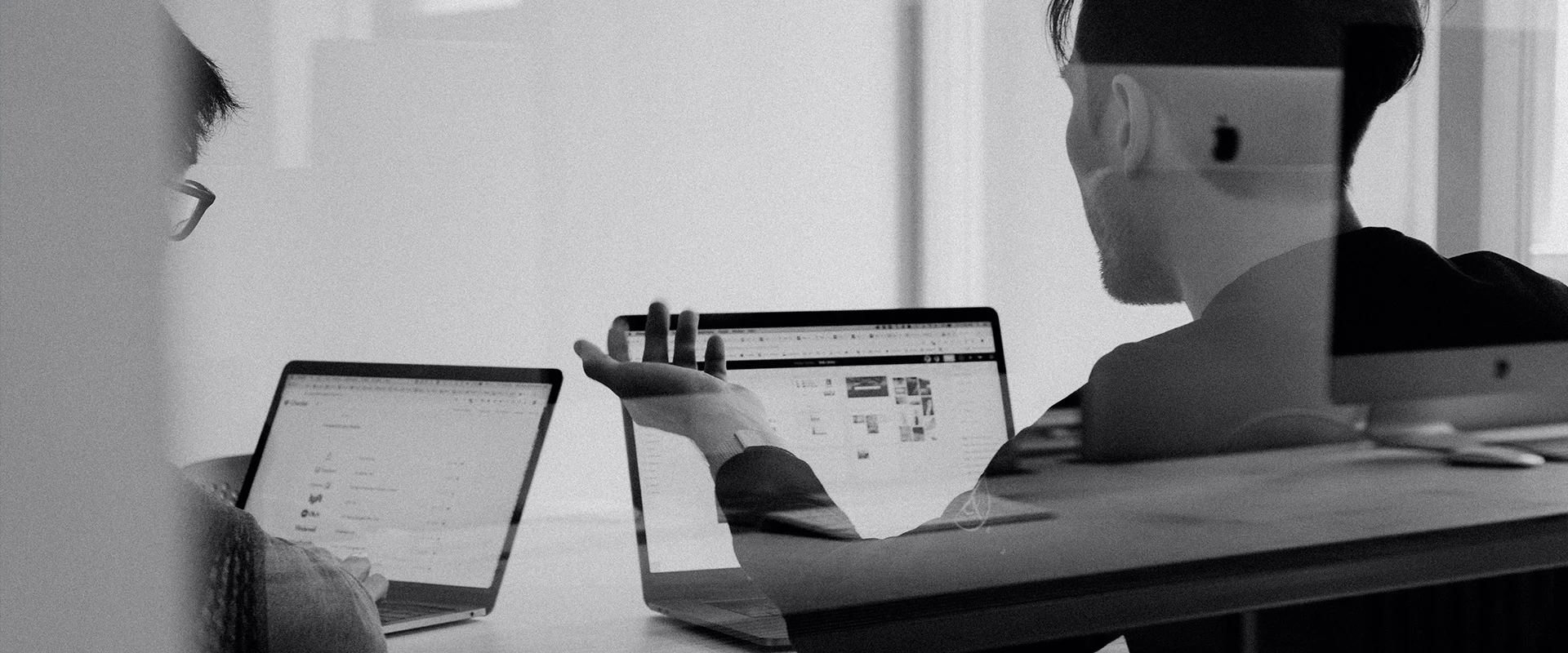 Ein Schwarz-Weiß-Foto, das zwei Personen zeigt, die mit Laptops Wachstumsmarketing-Aufgaben erledigen.