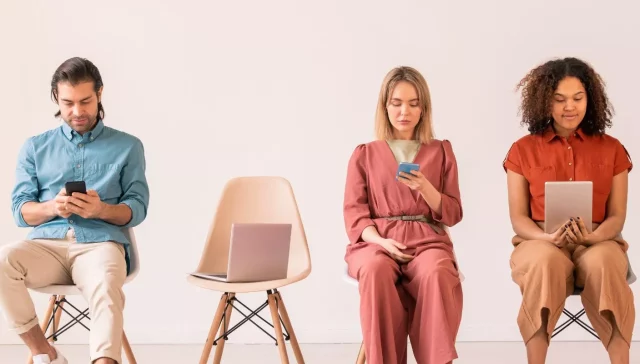 Eine Gruppe von Menschen, die auf Stühlen sitzen und mit ihren Telefonen auf Instagram surfen und gesponserte Werbung ansehen.