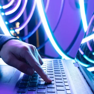 Eine Person, die eine Tastatur mit leuchtend blauer und violetter LED-Beleuchtung im Hintergrund verwendet.