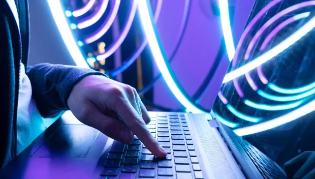 Eine Person, die eine Tastatur mit leuchtend blauer und violetter LED-Beleuchtung im Hintergrund verwendet.