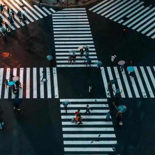 Luftaufnahme eines belebten Fußgängerübergangs mit Menschen, die die Straße in verschiedene Richtungen überqueren, was ein perfektes Szenario für die Zielgruppenanalyse darstellt.