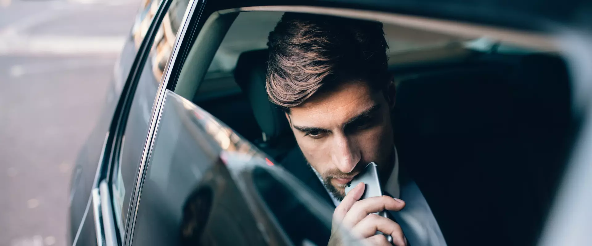 Ein Mann mit ernster Miene blickt auf sein Telefon, während er auf dem Rücksitz eines Autos sitzt und die Customer Journey für sein B2B-Unternehmen analysiert.
